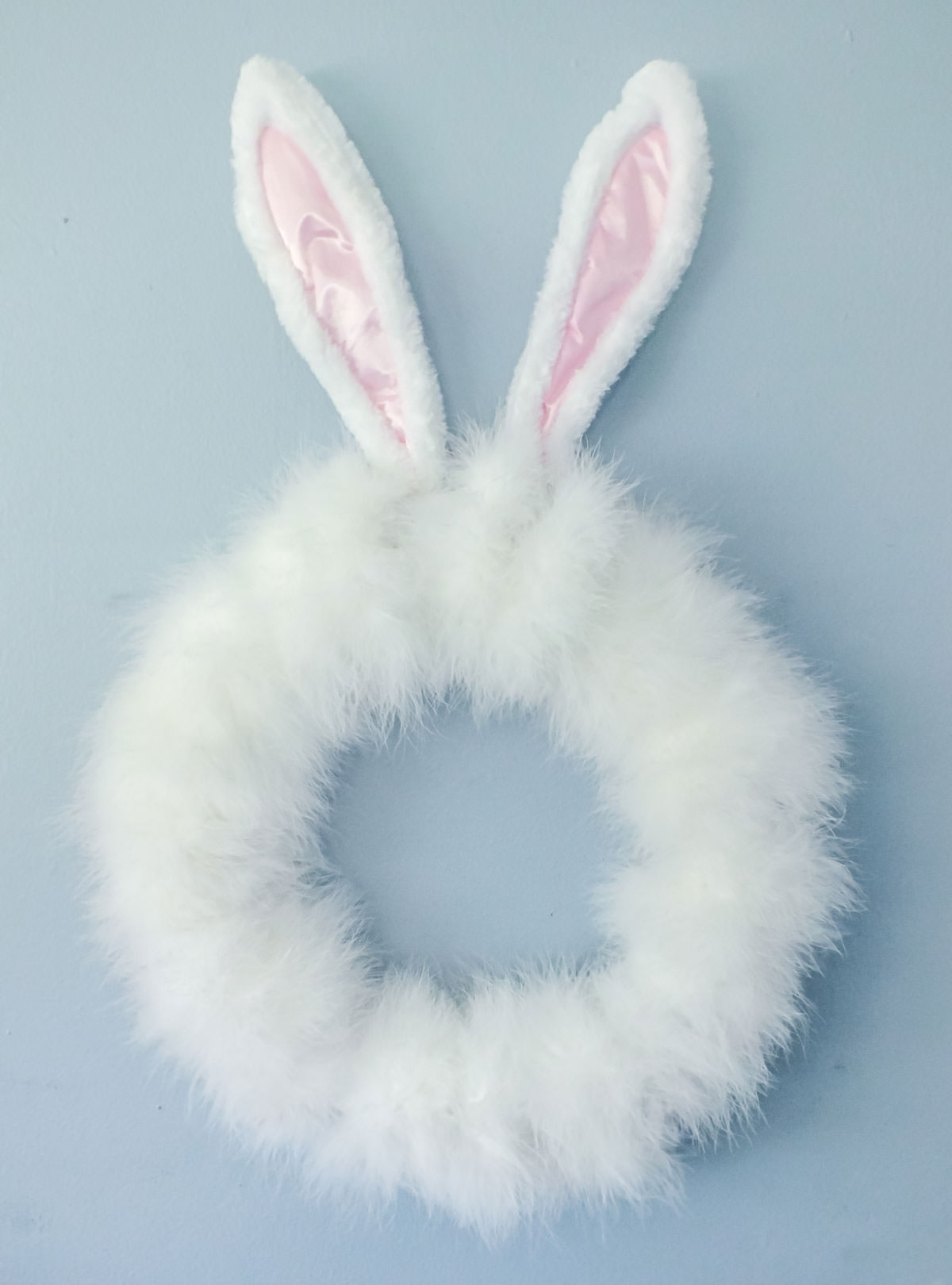 Closeup image of a DIY Easter Bunny Wreath hanging on a blue wall.