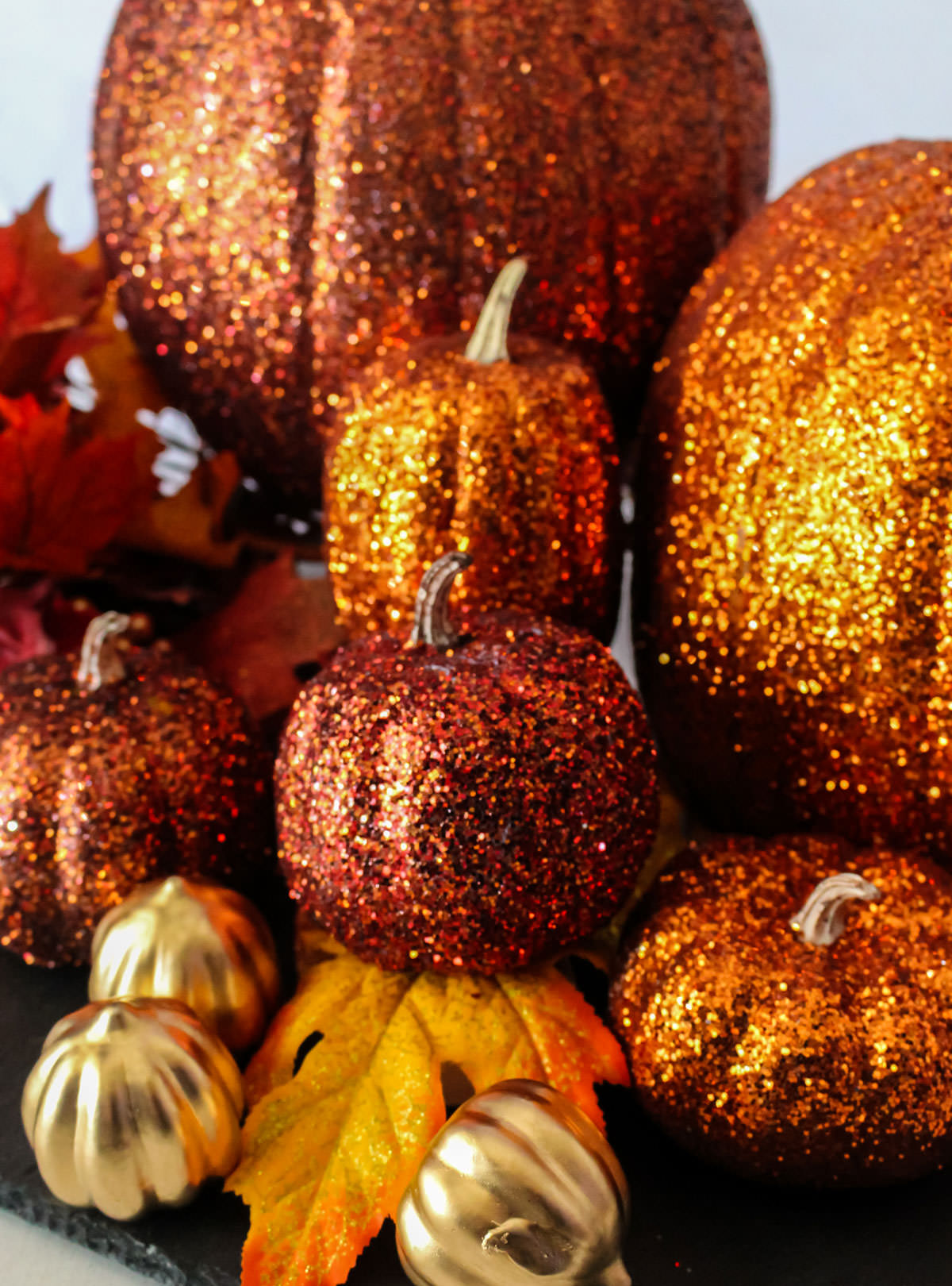 Closeup on a stack of Orange DIY Glitter Pumpkins of various sizes sitting on a black surface.