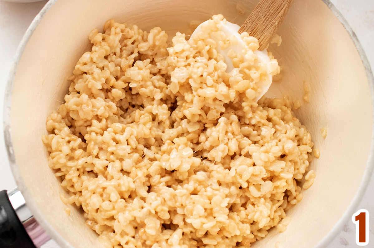 Closeup on a white sauce pan filled with warm Rice Krispie Treat mixture and a white wooden spoon.