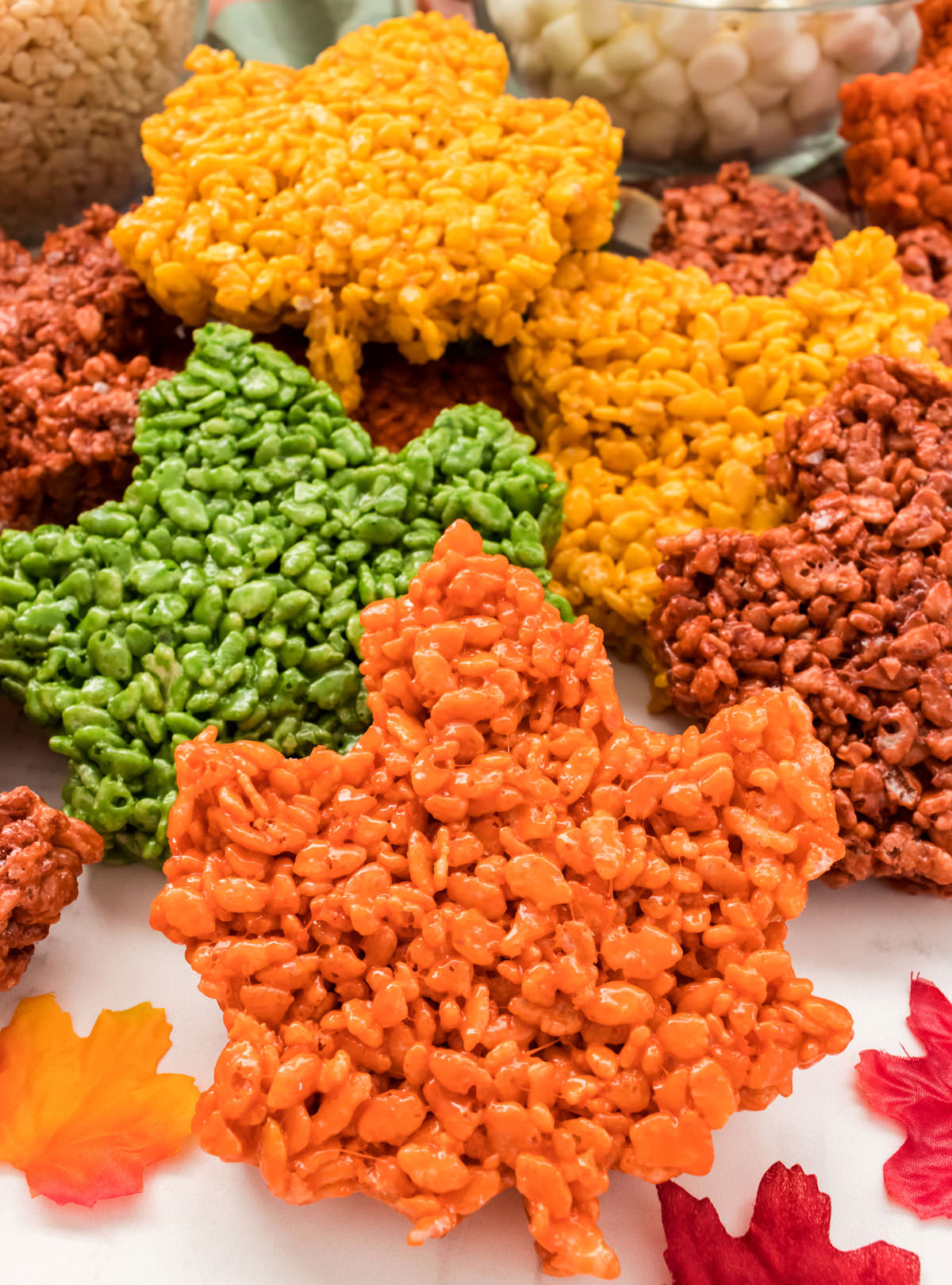 Closeup on a batch of Fall Leaves Rice Krispie Treats arranged on a white table surrounded by Autumn leave decorations.