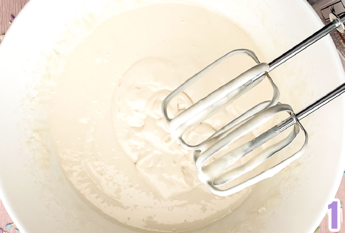 Closeup on a large white mixing bowl filled with white cake batter and a hand-mixer.