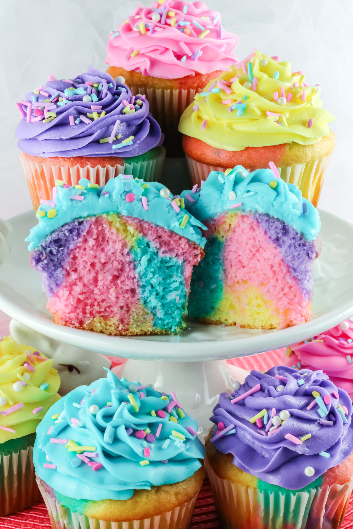 Closeup on a party display of Celebration Marble Cupcakes - including one cupcake cut in half to show the pastel marble pattern on the inside of the cupcake.