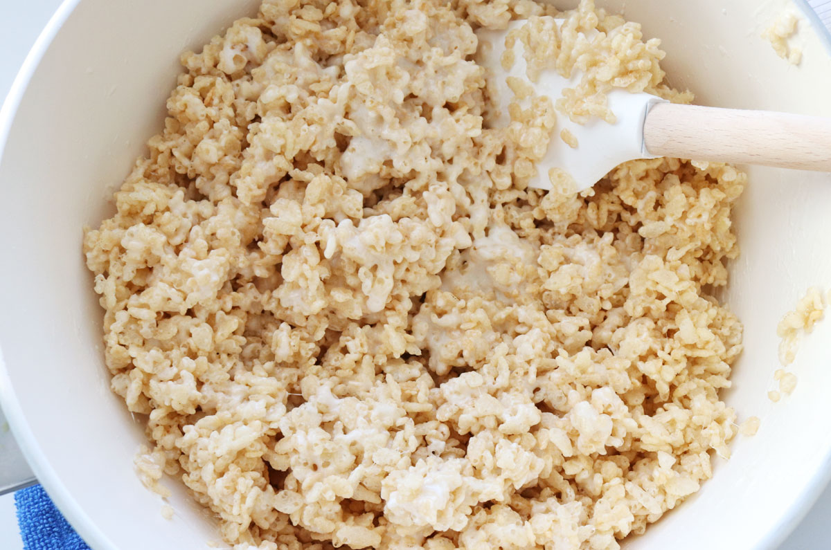 Close up on a white pan filled with Rice Krispie Treat mixture and a white wooden spoon.