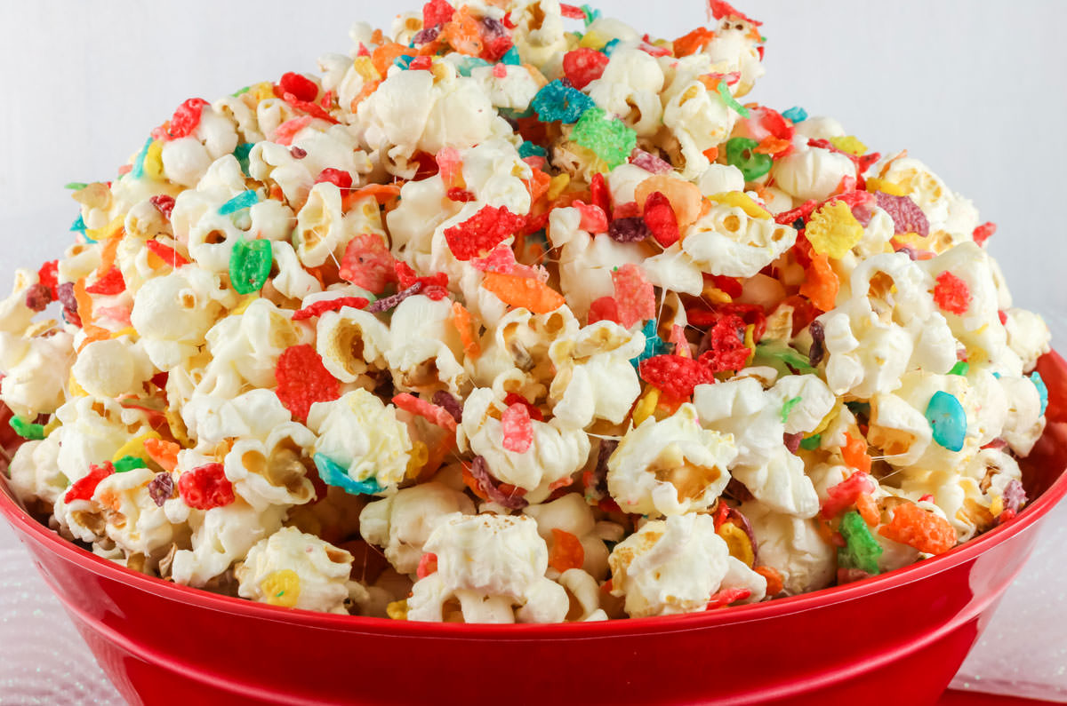 Closeup on a red serving bowl filled with Fruity Pebbles Popcorn sitting on a white table.