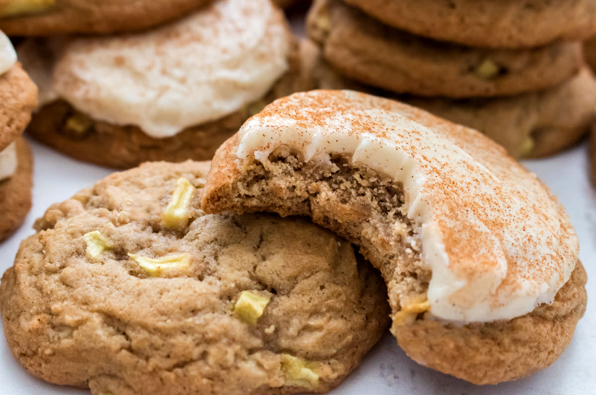 Closeup on two Apple Cookies with Cream Cheese Frosting (one frosted, one not frosted) laying on a white surface.