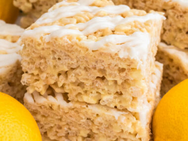 Picture of two Lemon Rice Krispie Treats sitting on a white table surrounded by Fresh Lemons.