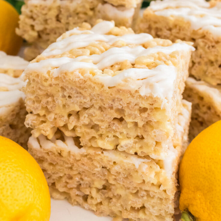 Picture of two Lemon Rice Krispie Treats sitting on a white table surrounded by Fresh Lemons.