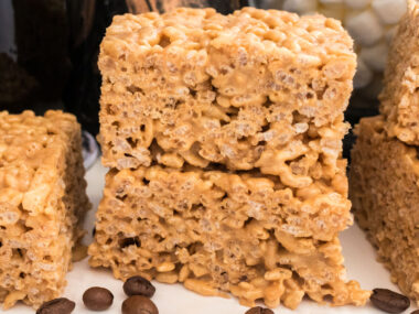 Closeup on a stack of two Coffee Rice Krispie Treats sitting on a white table in front of coffee beans.