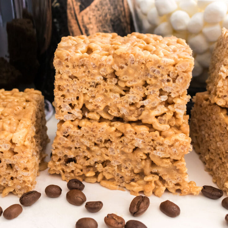 Closeup on a stack of two Coffee Rice Krispie Treats sitting on a white table in front of coffee beans.