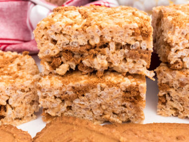 A batch of Cookie Butter Rice Krispie Treats sitting on a white table in front of Biscoff Cookies.