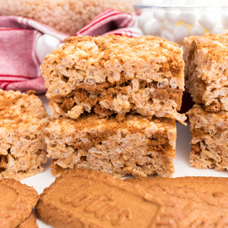 A batch of Cookie Butter Rice Krispie Treats sitting on a white table in front of Biscoff Cookies.