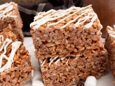 A stack of two Mocha Rice Krispie Treats sitting on a white dessert plate next to a glass cup filled with Mocha Coffee.