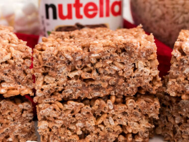 A batch of Nutella Rice Krispie Treats sitting on a white table alongside a jar of Nutella spread.