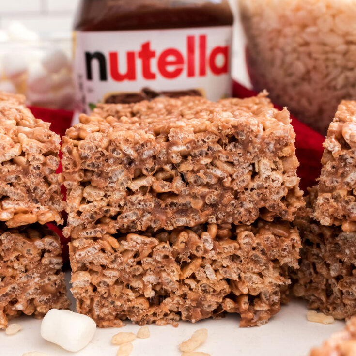 A batch of Nutella Rice Krispie Treats sitting on a white table alongside a jar of Nutella spread.