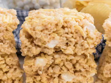 A batch of Potato Chip Rice Krispie Treats sitting on a white table in front of a handful of Ruffles Potato Chips.