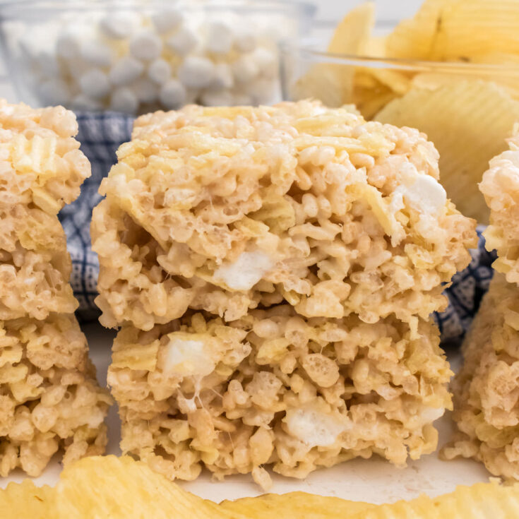 A batch of Potato Chip Rice Krispie Treats sitting on a white table in front of a handful of Ruffles Potato Chips.