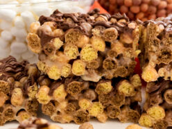 A batch of Reese's Puffs Marshmallow Treats sitting on a white table in front of clear bowls filled with marshmallows and cereal.