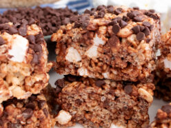 A batch of Zebra Rice Krispie Treats sitting on a white table surrounded by clear bowls full of cereal and marshmallows.