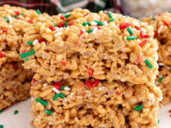 A stack of two Gingerbread Rice Krispie Treats sitting on a white table surrounded by Christmas sprinkles.