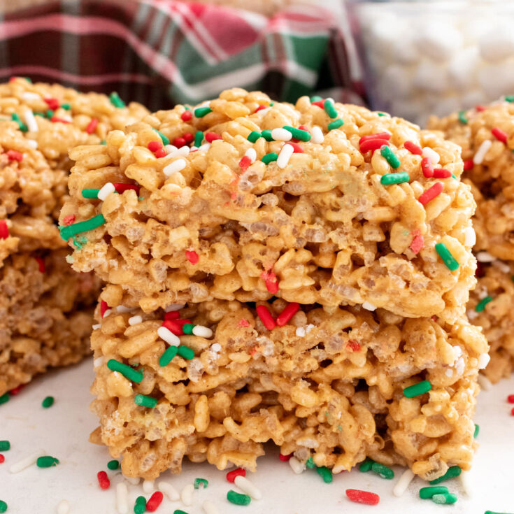 A stack of two Gingerbread Rice Krispie Treats sitting on a white table surrounded by Christmas sprinkles.