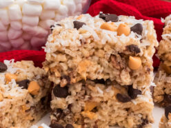 A stack of two Magic Bar Rice Krispie Treats sitting on a white table surrounded by Butterscotch Chips, Chocolate Chips and Coconut.