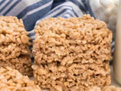 A stack of two Maple Rice Krispie Treats sitting on a white white in front of a blue striped kitchen towel.