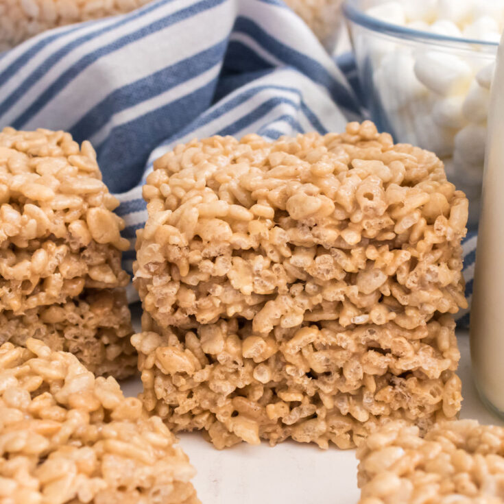 A stack of two Maple Rice Krispie Treats sitting on a white white in front of a blue striped kitchen towel.