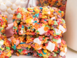 Closeup on a stack of two Fruity Pebbles Marshmallow Treats sitting on a white table next to a class of milk.