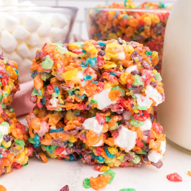 Closeup on a stack of two Fruity Pebbles Marshmallow Treats sitting on a white table next to a class of milk.