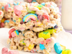 Closeup on a stack of two Lucky Charms Marshmallow Treats sitting on a white dessert plate next to a glass of milk.