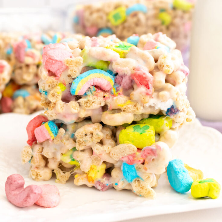 Closeup on a stack of two Lucky Charms Marshmallow Treats sitting on a white dessert plate next to a glass of milk.