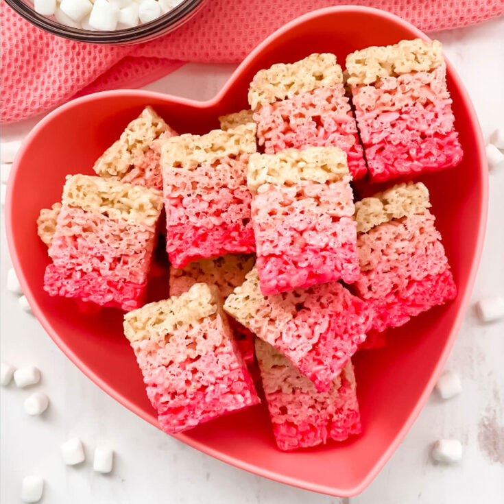 A batch of Ombre Rice Krispie Treats in a heart shaped bowl laying on a white table.