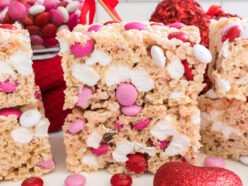 A stack of two Valentine's Day M&M Rice Krispie Treats sitting on a white table next to a glass bowl of M&M's.