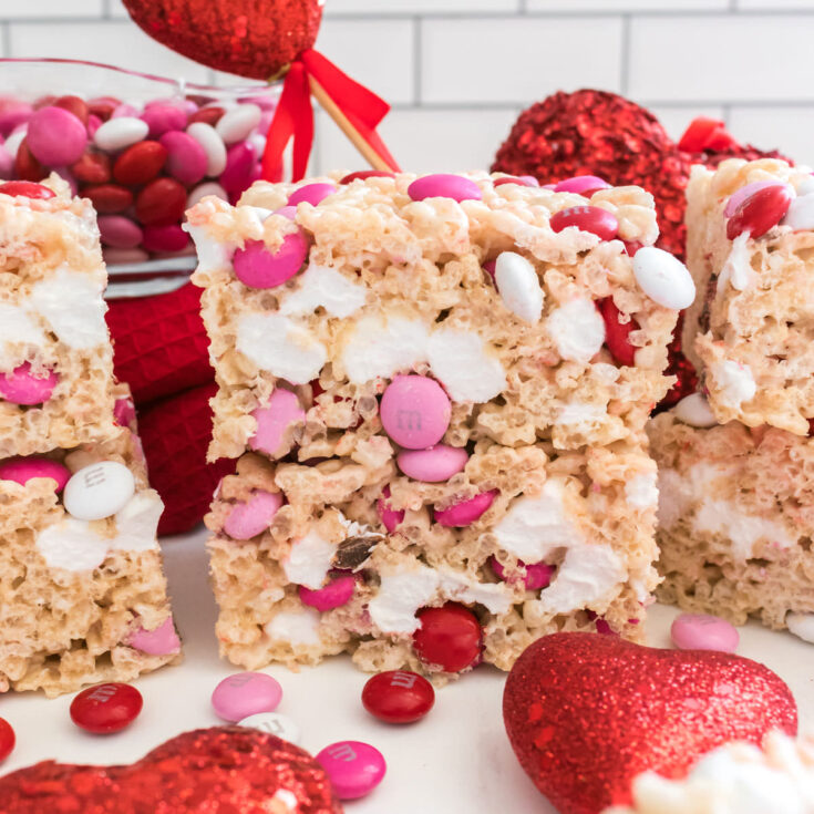 A stack of two Valentine's Day M&M Rice Krispie Treats sitting on a white table next to a glass bowl of M&M's.